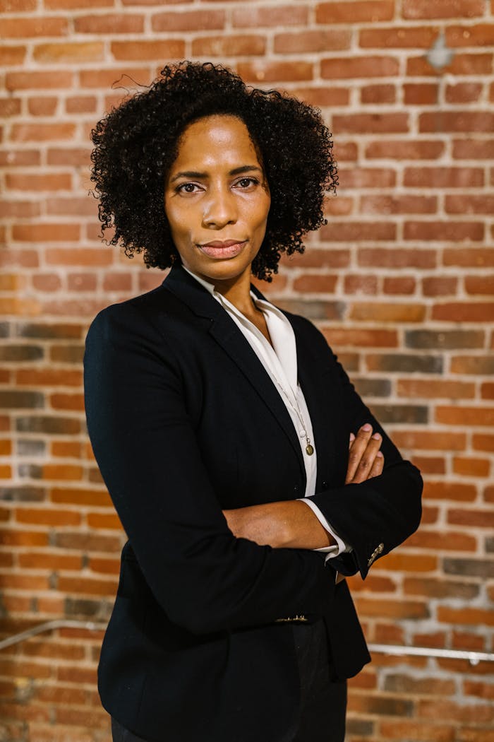 Portrait of a confident businesswoman in formal attire standing against a brick wall background.
